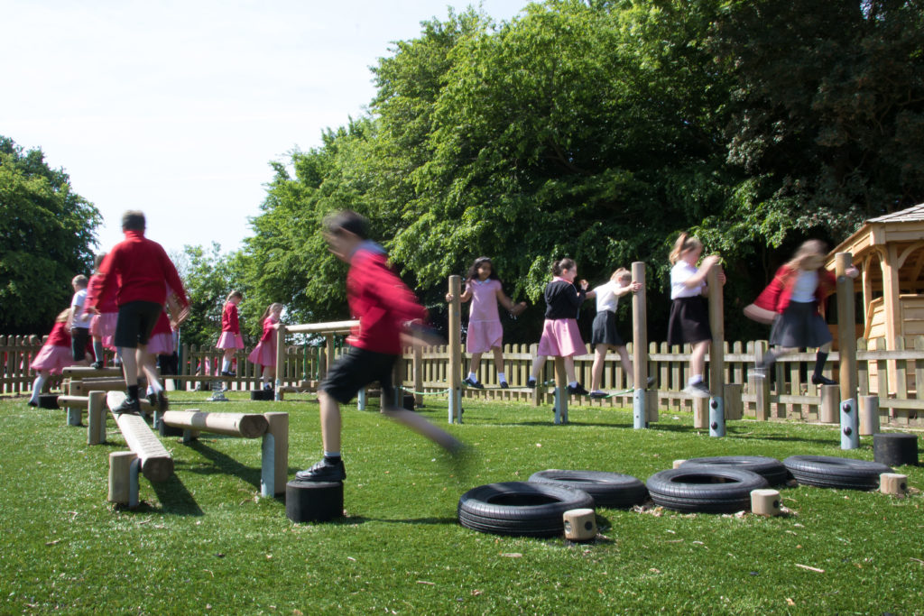 Pupils are pictured in the outdoor play area, traversing an obstacle course.