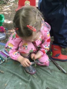 A young girl from the Nursery is seen making a stick man using sticks in the Forest School.