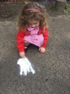 A young girl from the Nursery is seen drawing Dinosaur footprints on the ground.