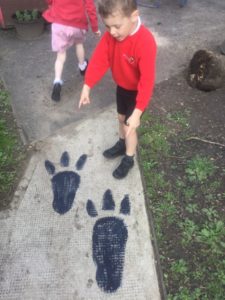A young boy from Nursery points to a pair of Dinosaur footprints on the ground.