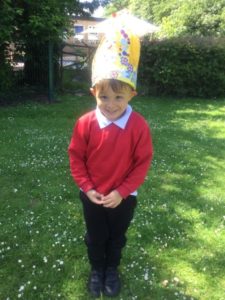 A young Nursery boy can be seen posing for the camera on the school grounds, wearing a hat he has created in celebration of the Queen's Platinum Jubilee.