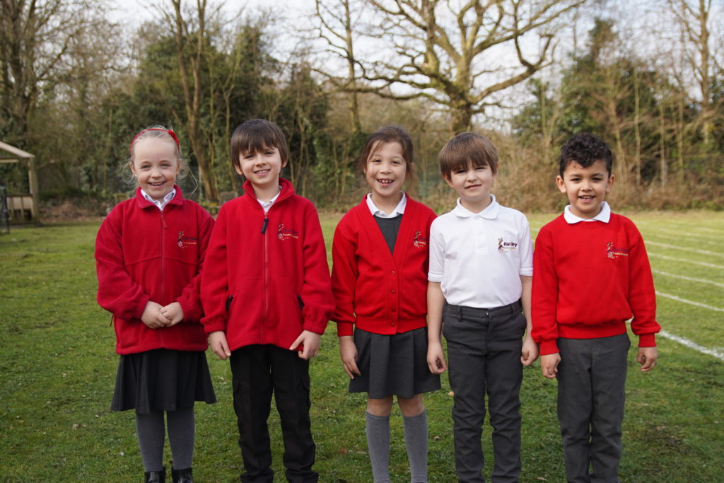 Five pupils, three boys and two girls, can be seen standing outdoors on the academy grounds, wearing their uniforms and smiling for the camera.